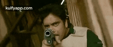 a man is pointing a gun at the camera and looking at the camera .