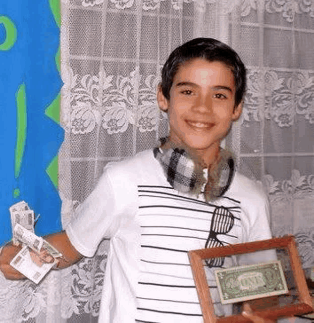 a young boy is holding a framed picture of a dollar bill and a bunch of money .