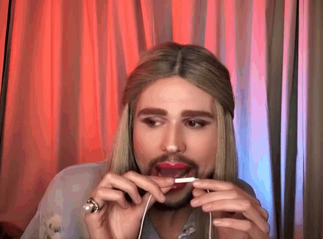a man with long blonde hair and a beard is holding a cigarette in his mouth