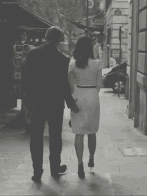 a black and white photo of a man and woman walking down a sidewalk