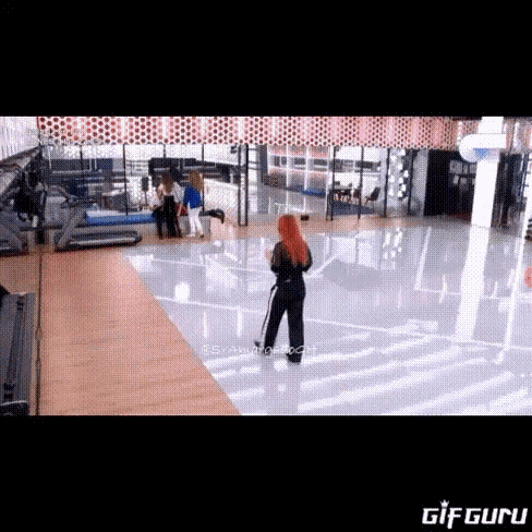 a woman with red hair is standing in a gym cleaning the floor with a mop .