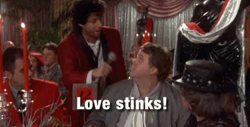 a man in a red jacket is talking into a microphone and says love stinks