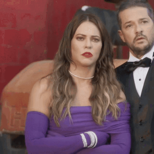 a woman in a purple dress and gloves is standing next to a man in a tuxedo