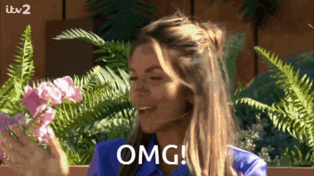 a woman in a blue shirt says omg in front of flowers and ferns