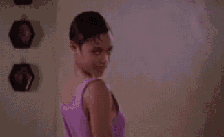a woman in a purple tank top is standing in front of a mirror and touching her nose .
