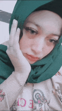 a woman wearing a green head scarf and a bracelet with the letter e on it