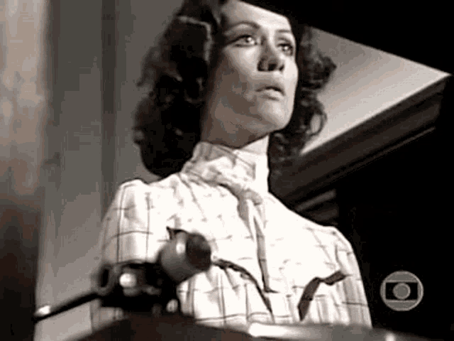 a woman in a plaid shirt is standing in front of a piano and looking at the camera .