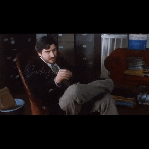 a man in a suit and tie is sitting in a chair with his legs crossed and the words suday on the bottom