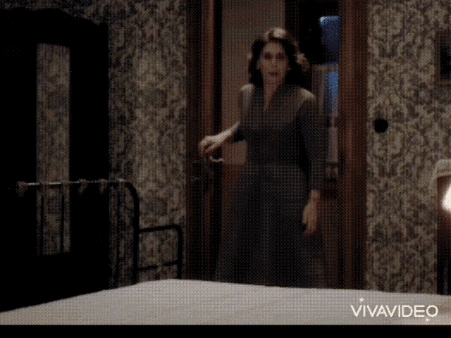 a woman in a dress is standing next to a bed in a room with a vivavideo logo on the bottom
