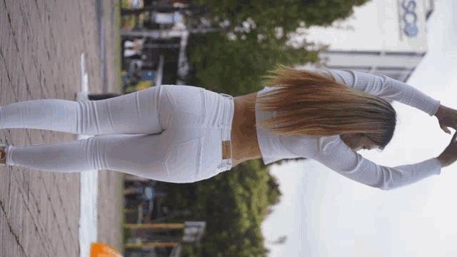 a woman in white pants and a crop top stretches her arms