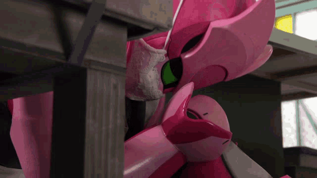 a pink robot with a green eye is sitting under a wooden table