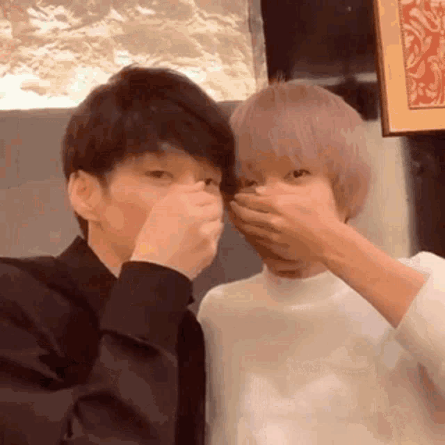 two men are covering their mouths with their hands while sitting next to each other .
