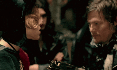 a man in a leather jacket is holding a gun in front of a woman