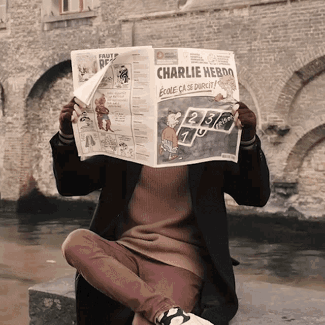 a person holding a newspaper with charlie hebdo on the front