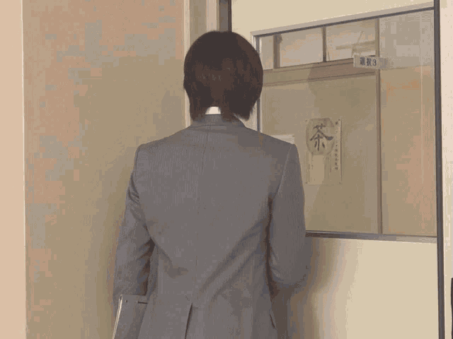 a woman in a suit stands in front of a door that has a sign on it that says 3