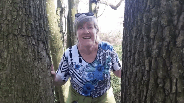 a woman in a blue and white shirt smiles between two trees