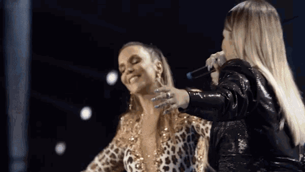 a woman in a leopard print top is smiling while another woman holds a microphone