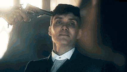 a man in a suit and tie is being shot with a gun to his head .