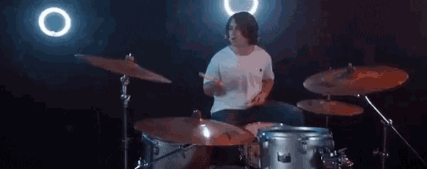 a man is playing drums in a dark room with a ring light in the background .