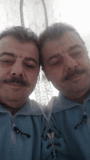 a man with a mustache is taking a selfie with his reflection in a mirror