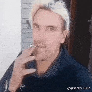 a man with blonde hair is smoking a cigarette and making a funny face .