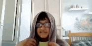 a young boy wearing glasses and a hoodie is holding a piece of paper in front of his face .