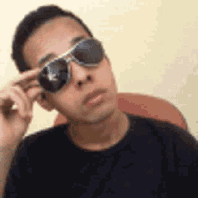 a man wearing sunglasses is sitting in a chair looking at the camera .