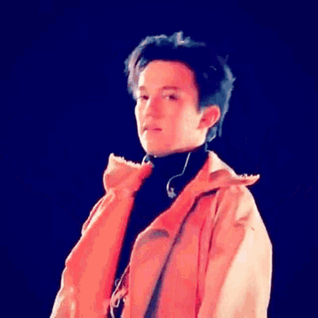 a man in a red jacket is standing in front of a microphone and covering his mouth with his hand .