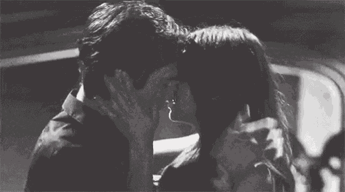 a black and white photo of a man and a woman kissing in a car .