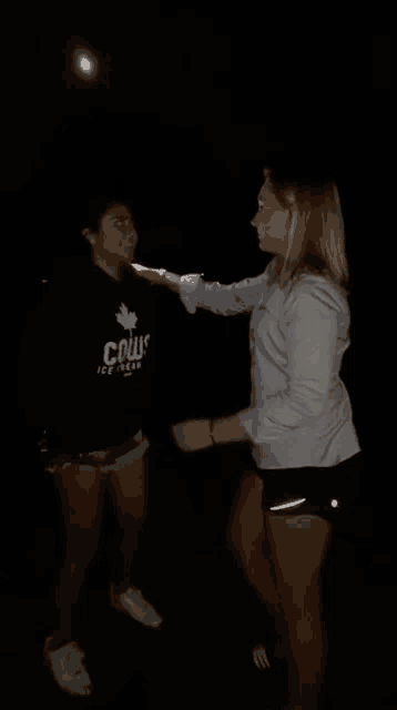 a woman wearing a cows ice cream shirt is standing next to another woman in shorts