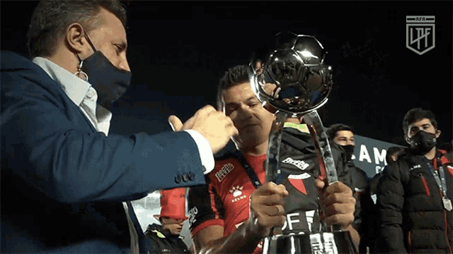a man wearing a mask holds a trophy in front of a sign that says ltf