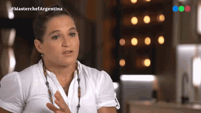 a woman in a white shirt is talking on a television screen with the hashtag #masterchefargentina
