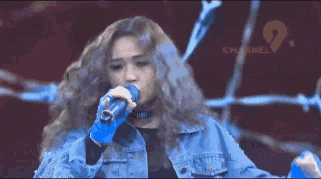 a woman singing into a microphone with a channel 9 logo behind her
