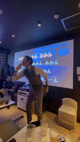 a man singing into a microphone in front of a large screen that says ' みかん ' on it