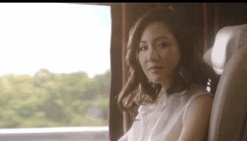 a woman in a white shirt is sitting in a car looking out the window .
