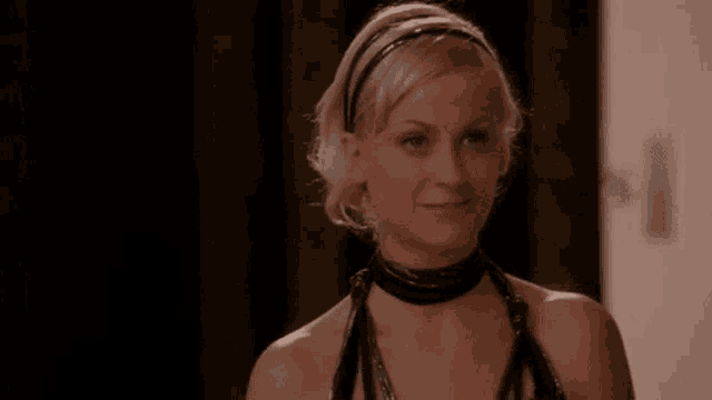 a woman wearing a black choker and a headband is smiling and looking at the camera .