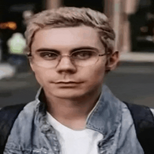 the man is wearing glasses and a denim jacket .