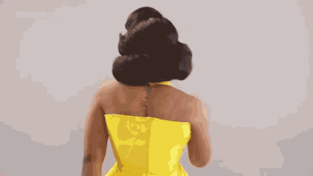 a woman in a yellow dress with a tattoo on her back is standing with her back to the camera .