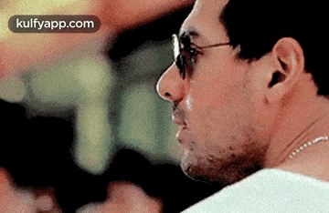 a man wearing sunglasses and a chain around his neck is looking to the side .