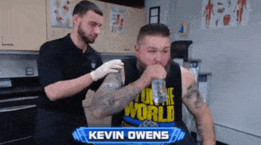 a man in a tank top that says kevin owens drinks from a bottle