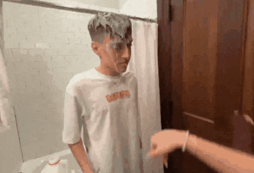 a man in a white shirt is covered in a white substance while standing in a bathroom