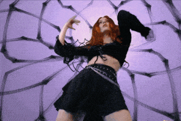 a woman with red hair is dancing in front of a purple and black background