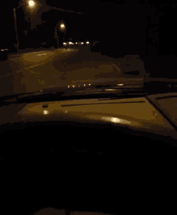 a car is driving down a street at night with a street light in the background