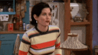 a woman is standing in a kitchen wearing a striped sweater and a lamp .