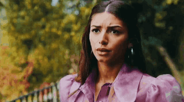 a woman in a purple dress is standing in front of a fence and looking at the camera .