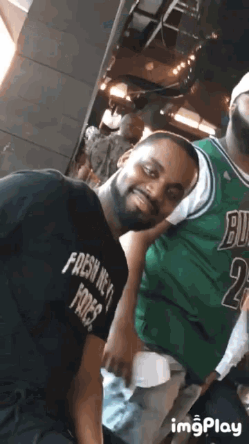 a man wearing a black shirt that says fresh new fries stands next to another man wearing a green jersey that says bulls