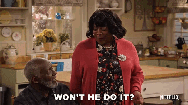 a woman in a red sweater says " won 't he do it " next to an older man in a kitchen