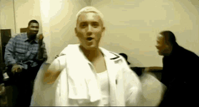 a man with a towel around his neck is standing in a room with two other men .