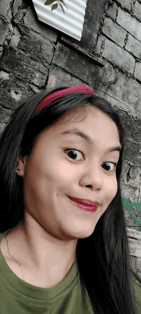 a young girl wearing a headband makes a funny face in front of a brick wall