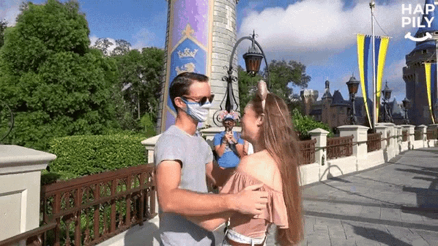 a man and a woman are kissing in front of a castle . the man is wearing a mask .